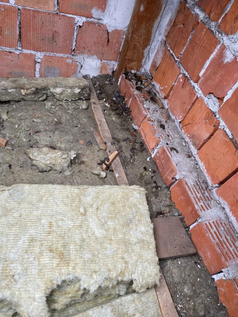 Uszkodzona wełna mineralna i zanieczyszczenia przy murowanej ścianie poddasza